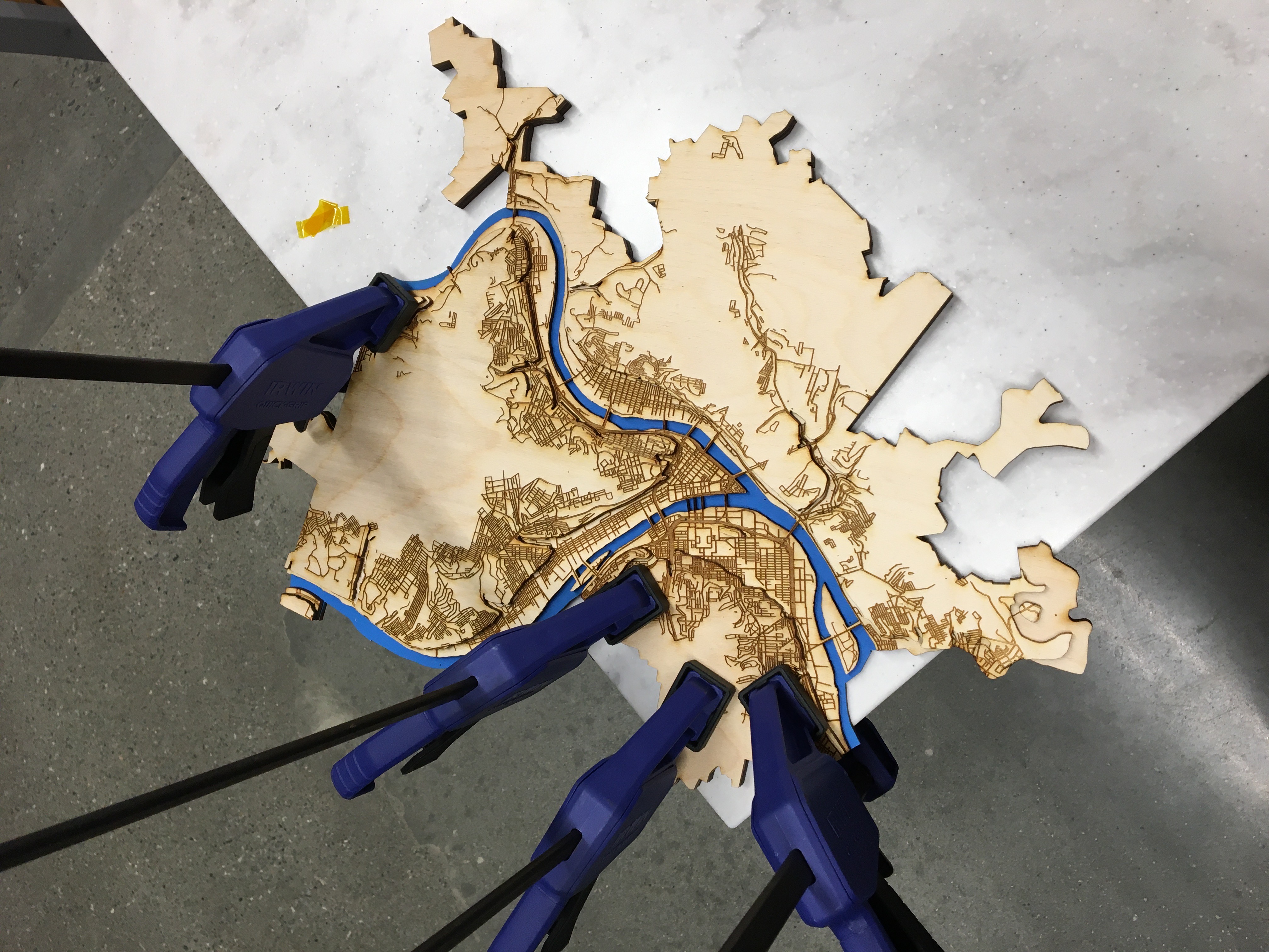 An in-progress laser cut wooden topographic map, held by clamps to a tabletop