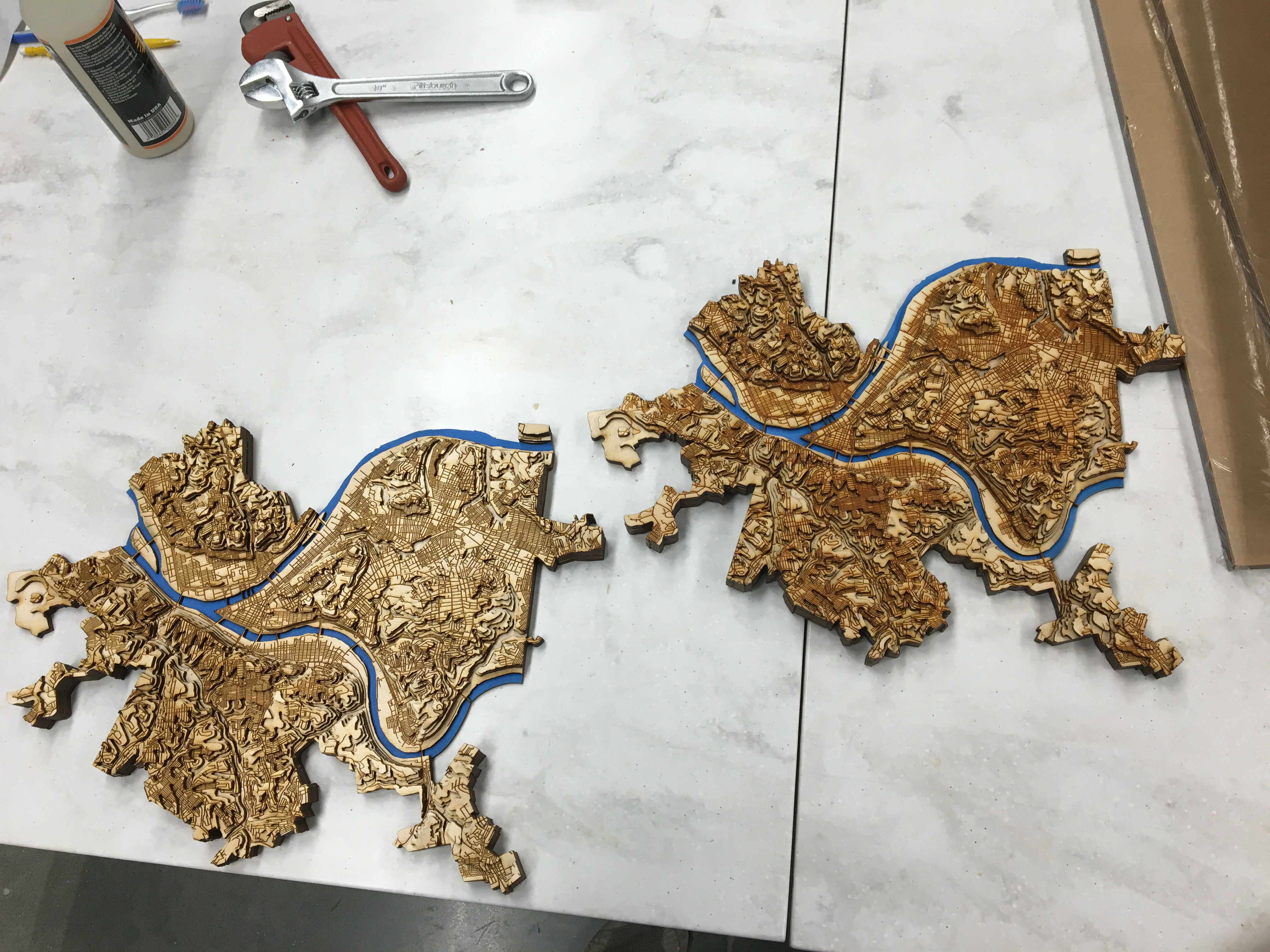 Two topographic maps side by side on a table. The one on the left is lighter and has less contrast than the one on the right.