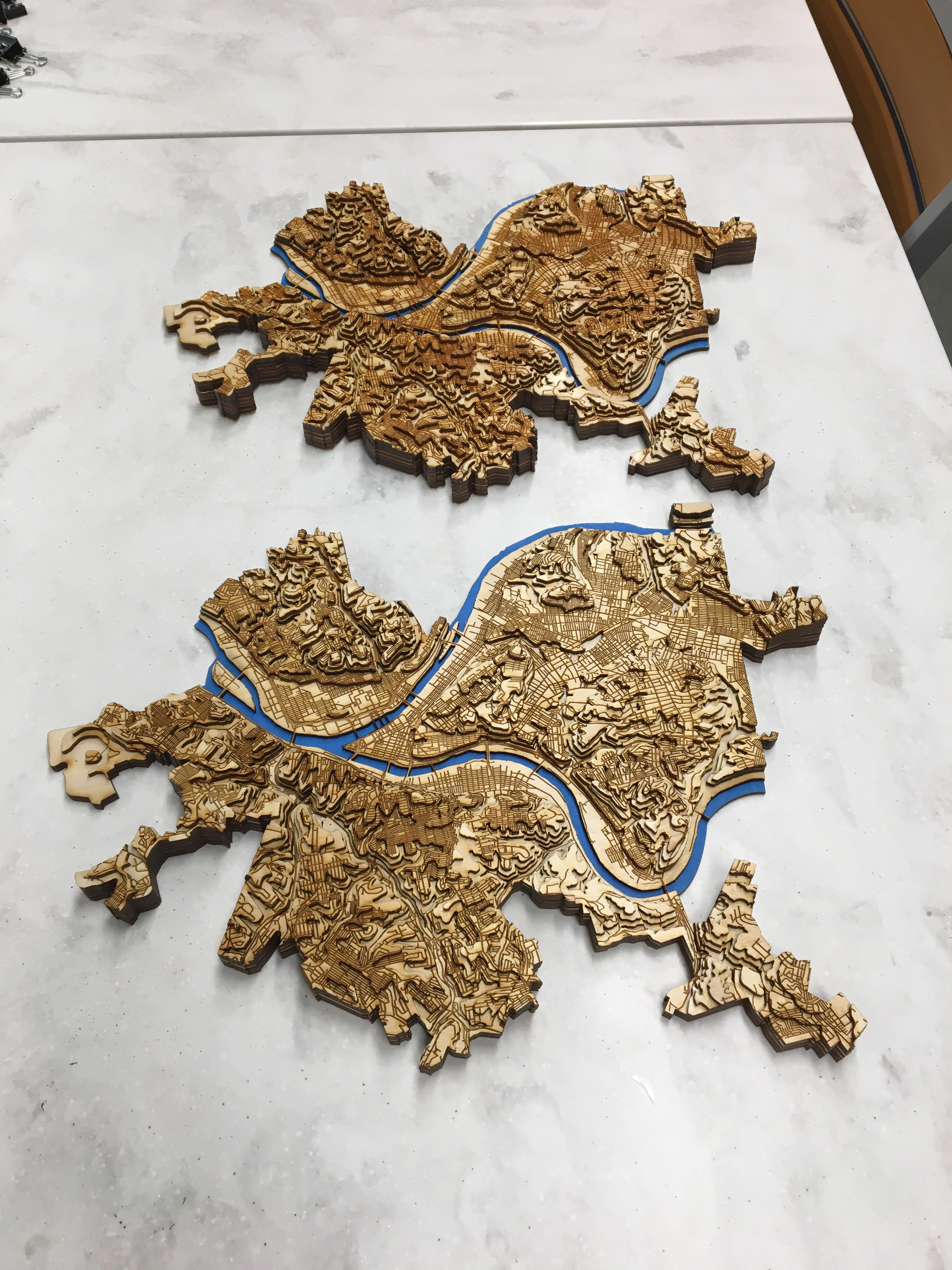 Two topographic maps on a table. One is closer to the camera and is lighter than the other.